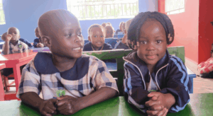 schulkinder-klassenraum-buwooya-uganda Zwei Kinder der Fransalian Vorschule sitzen gemeinsam an einem grünen Tisch im Klassenraum.